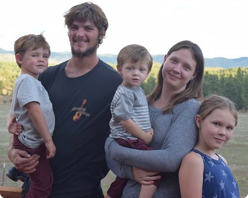 Happy family of five posing outdoors with mountains in the background.