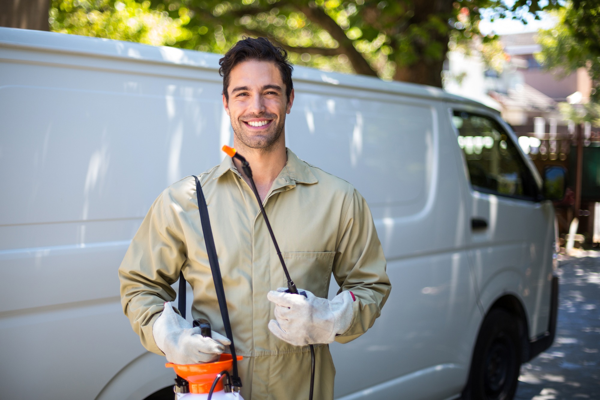 Portrait of smiling worker with pesticide sprayer while standing by van